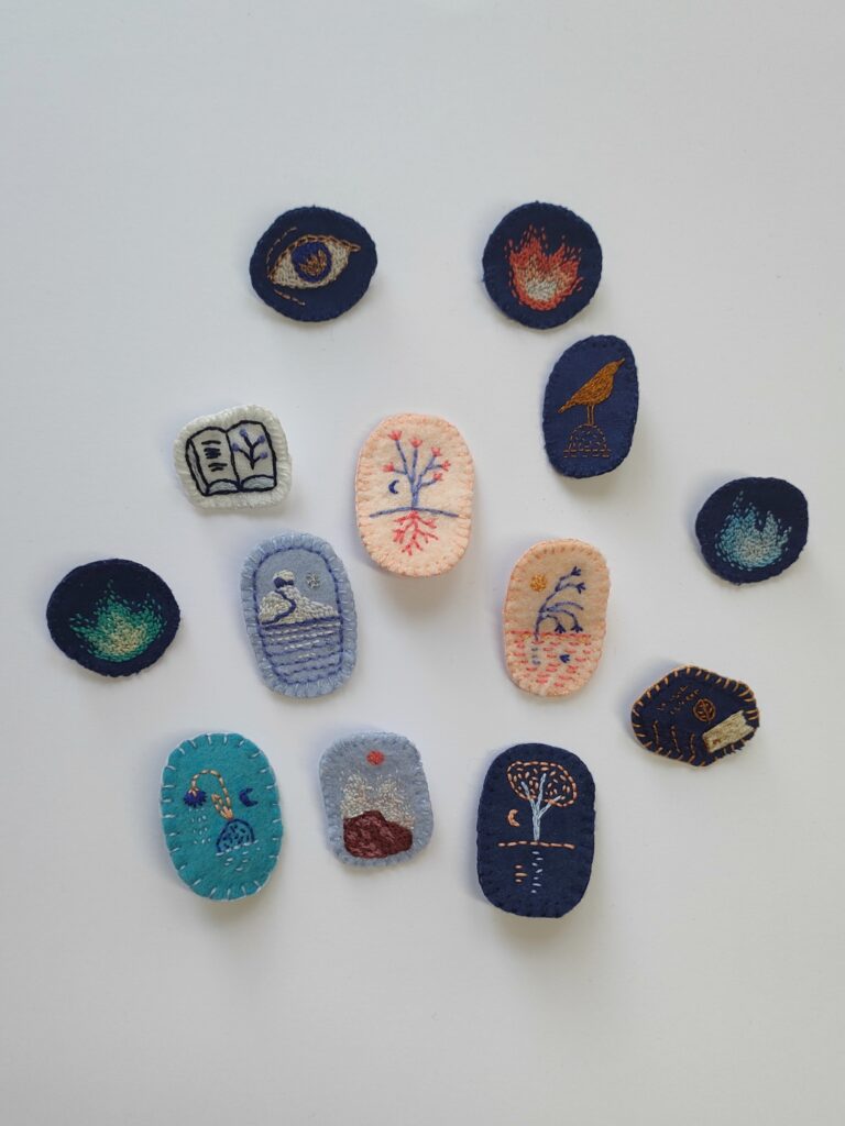 Vue d'ensemble de 13 petites broches brodées sur du tissu ou de la feutrine.